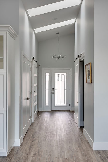 A long elegant hallway with two roof panels allowing in lots of natural light. A hanging light in near the door at the end.