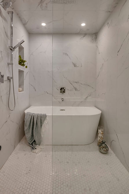 A light and minimal bathroom with a beautiful bathtub on the back wall, a shower on the left, and a glass shower pane in the foreground.