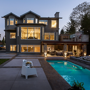 A stunning photo of a newly renovated house in Canada, early in the evening with lights on and a swimming pool